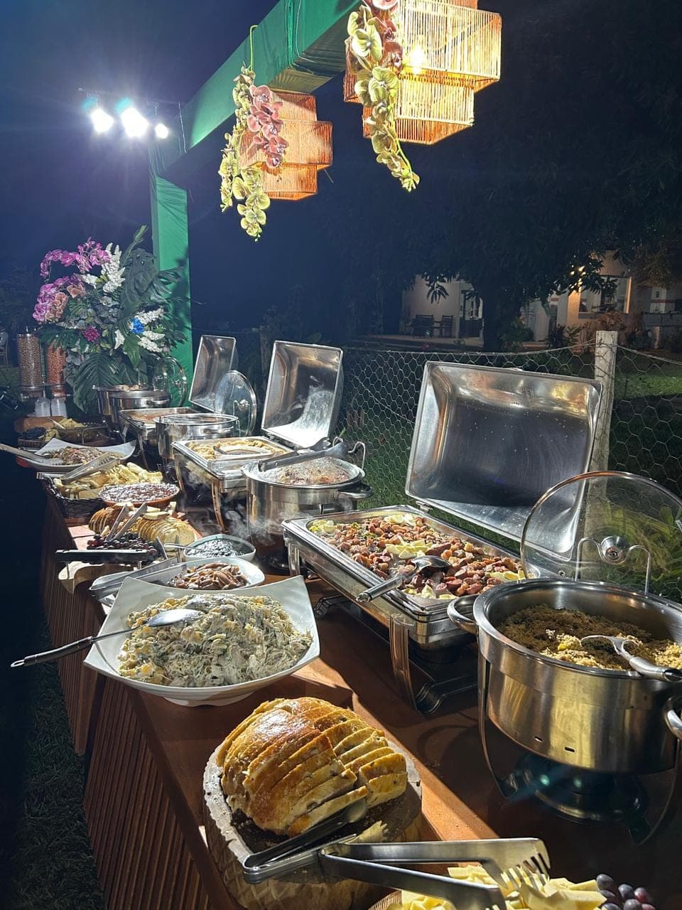 Buffet montado ao ar livre para evento noturno, com iluminação quente sobre as travessas